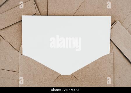 Blank white paper is placed on the open brown paper envelope. Mock-up of horizontal blank greeting card. Top view of Craft paper envelope on white bac Stock Photo