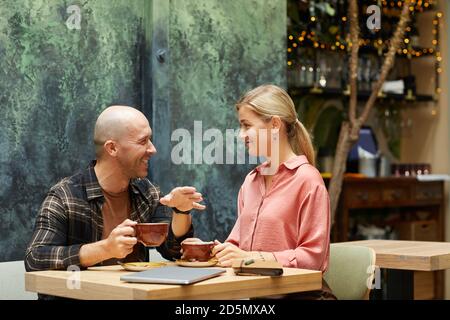 Young couple sitting at the table and talking to each other while drinking coffee in coffee shop Stock Photo