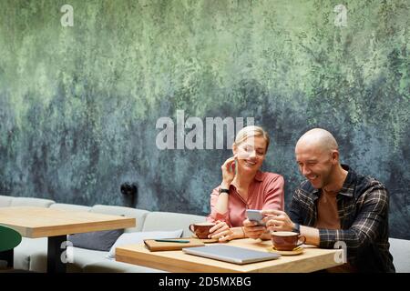 Young man using mobile phone while drinking coffee in cafe together with his girlfriend Stock Photo