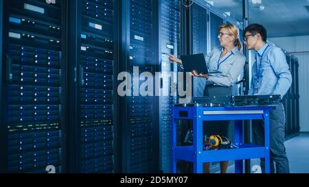 In the Modern Data Center: Engineer and IT Specialist Work with Server Racks, on a Pushcart Equipment for Installing New Hardware. Specialists Doing Stock Photo
