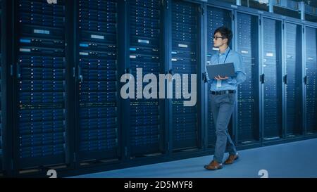 In the Modern Data Center: IT Engineer Working with Server Racks, Uses Laptop for Maintenance and Diagnostics. Checking Stability of the System Stock Photo