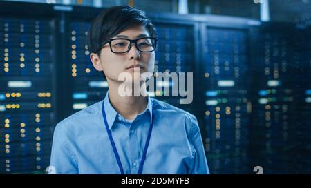 In the Modern Data Center: Portrait of IT Engineer Working With Touch Screen Device. In the Background Working Server Racks with Blinking LED Lights. Stock Photo