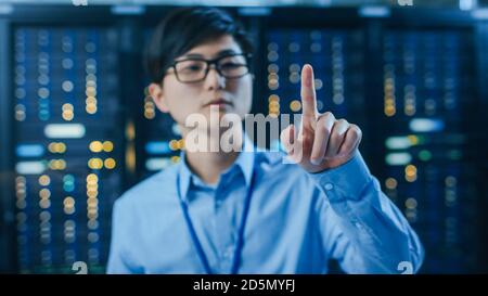 In the Modern Data Center: Portrait of Asian IT Engineer Working With Touch Screen Device, Doing Touching Gesture. In the Background Working Server Stock Photo