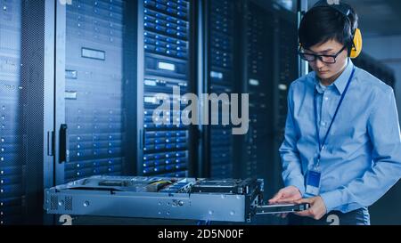 In the Modern Data Center: IT Technician Working with Server Racks, on a Pushcart Installing New Hardware. Engineer Doing Maintenance and Diagnostics Stock Photo