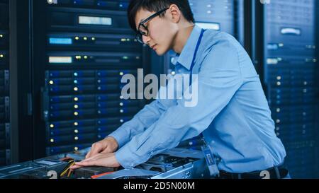 In the Modern Data Center: IT Technician Working with Server Racks, on a Pushcart Installing New Hardware. Engineer Doing Maintenance and Diagnostics Stock Photo