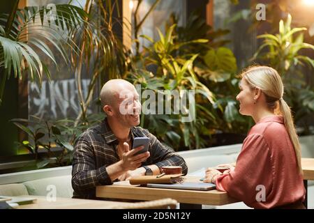 Smiling young man talking to young woman at the table in cafe Stock Photo