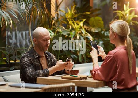Young couple using mobile phones at the table during meeting in internet cafe Stock Photo