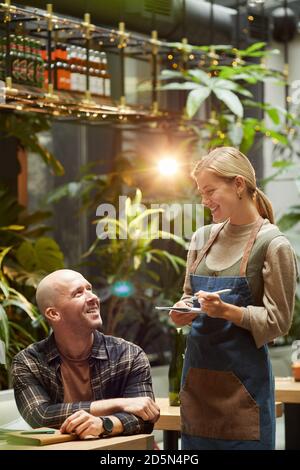 Young waiter taking an order from the young man while he sitting at the table in cafe Stock Photo