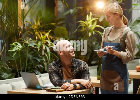 Businessman making an order to the waiter while working with laptop at the table in cafe Stock Photo
