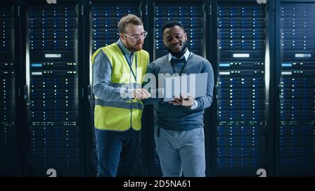 Bearded Black IT Engineer Standing and Smiling in the Middle of a Working Data Center Server Room with Server Computers Working on a Rack. Stock Photo