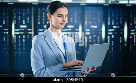 Female IT Specialist is Working on Laptop in Data Center Next to Server Racks. Stock Photo