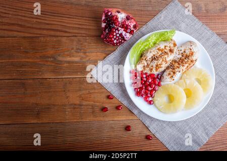 Fried chicken fillets with lettuce, pineapple and pomegranate seeds on brown wooden background, copy space, top view. Stock Photo