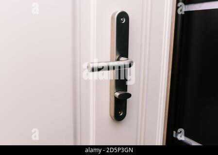 White door and handle. Modern chrome handle in your hotel room or home. Entrance to an apartment, office, or bedroom. Detail of a wooden door