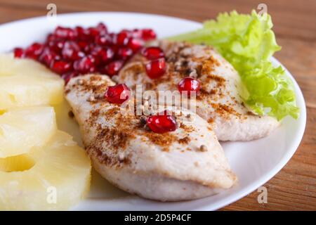 Fried chicken fillets with lettuce, pineapple and pomegranate seeds on brown wooden background, close up. Stock Photo