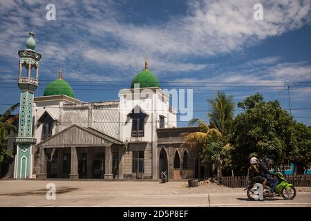 Horizontal shot of two people on a motorbike passing in front of a mosque, South Sulawesi, Indonesia Stock Photo