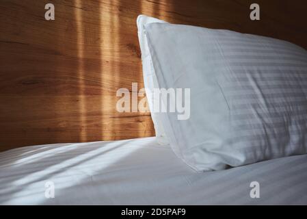 White pillow on bed in apartment bedroom with morning sunlight beaming through curtains Stock Photo