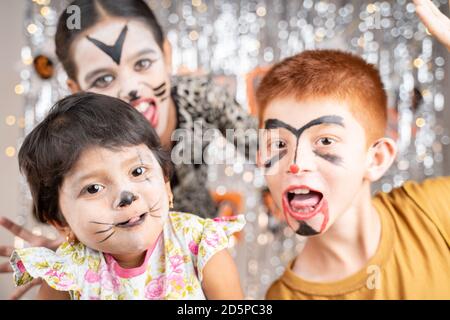 Group of kids in Halloween costumes gesticulating and making scary or spooky faces on decorated background by looking into camera. Stock Photo