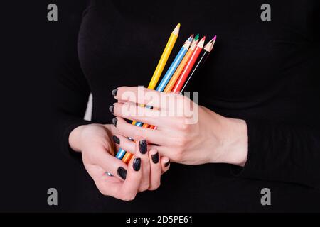 Female hands holding colored pencils on a black background. Manicure with black nail polish. Copy space Stock Photo