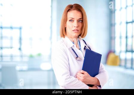 Female doctor holding folder in her hand while standing in exam room. Stock Photo