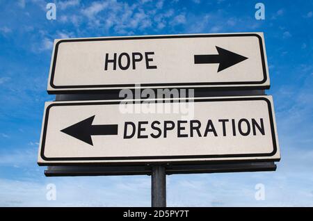 Hope vs desperation. White two street signs with arrow on metal pole with word. Directional road. Crossroads Road Sign, Two Arrow. Blue sky background