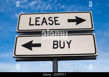 Lease vs buy. White two street signs with arrow on metal pole with word. Directional road. Crossroads Road Sign, Two Arrow. Blue sky background. Stock Photo