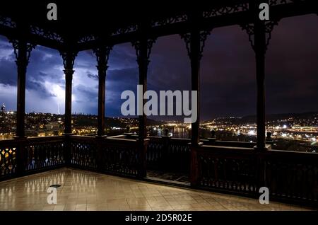 View of illuminated city during thunderstorm with lightning from wooden openwork gallery or gazebo in Prague, Czech Republic. Stock Photo