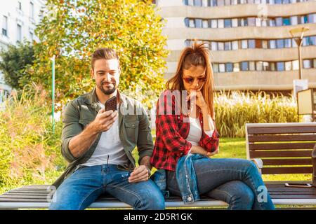 A girlfriend being annoyed by her boyfriends smartphone usage and bored. Stock Photo