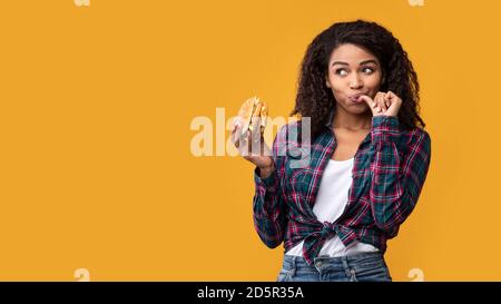 Happy African American Lady Holding Burger At Studio Stock Photo