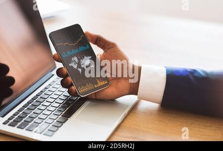 Black businessman checking global financial analytic on smartphone or trading on forex Stock Photo