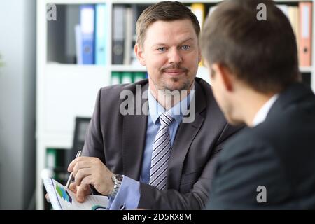 Man in business suit shows graph with pen on document at meeting with clients in office portrait Stock Photo
