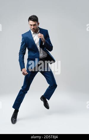 Full-length photo of funny man in suit running or jumping in air isolated over gray background. Stock Photo