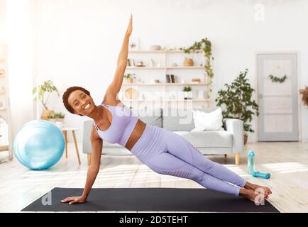 Millennial black woman doing side plank on yoga mat indoors Stock Photo