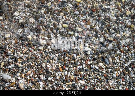 Pebbles and Foam. Beach pebbles and soft foam wave; sea stones background. Wet pebbles on sea coast Stock Photo