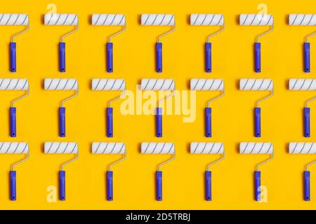 Pattern with paint roller with blue handle on yellow background. Clean roll for painting walls. Stock Photo