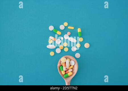 Colorful pills and capsules on a wooden spoon on a blue background,  pills are scattered in the center from bottom to top, isolated Stock Photo