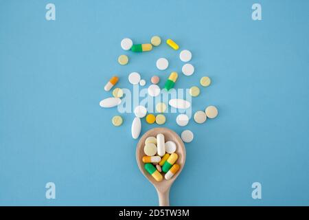Colorful pills and capsules on a wooden spoon on a blue background,  pills are scattered in the center from bottom to top, isolated Stock Photo