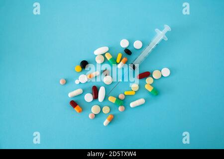 Multi-colored pills and capsules placed on a blue background with a syringe in the center of the conceptual image Stock Photo