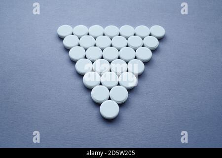 Round medicinal pills in the shape of a large triangle on a dark background, isolate. Stock Photo