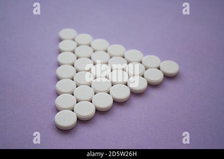 Round medicinal pills in the shape of a large triangle on a dark pink background, isolated. Stock Photo