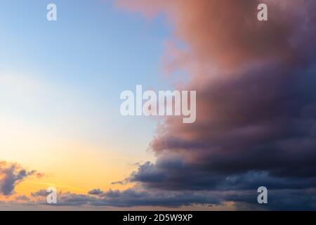 Golden azure evening sky is half covered by a dark reddish storm cloud. Calm before the storm, serenity after hurricane, light and dark confrontation. Stock Photo