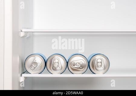 Four cans of beer or soda on the shelf in an empty home fridge. Cooling beverages in aluminum cans with pull tabs before drinking. Copy space. Stock Photo