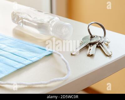 Medical face mask, hand sanitizer and set of three house keys on the ring over a table. Personal protection against viral infection when going outdoor Stock Photo