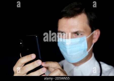 Doctor in mask using smartphone, mobile phone in male hand close up. Concept of appointment online, medical exam Stock Photo