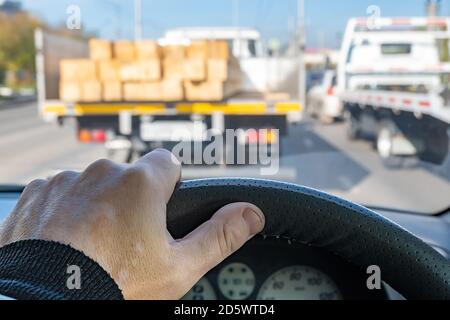 driver hand on the steering wheel of a car, in front of a truck with a dangerous cargo of lumber