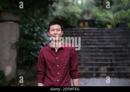 medium shot of one young smiling Asian man looking at camera. In natural park Stock Photo