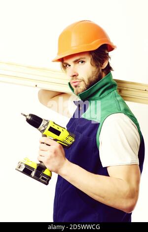 Construction worker holds wooden boards on shoulder and yellow drill. Builder in orange helmet and uniform. Finished work and building concept. Man with serious face, isolated on white background Stock Photo
