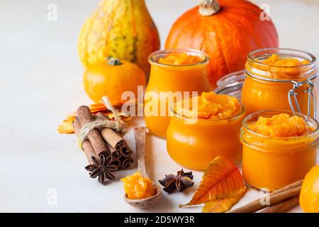 Pumpkin puree in different glass jars with spices and fresh pumpkins. Autumn or winter food. Light background. Stock Photo