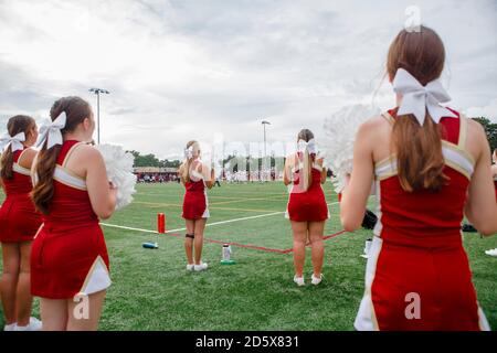 A group of cheerleaders with bows in hair stand on football field Stock Photo