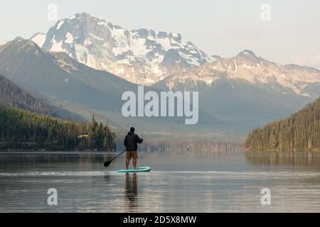 Back view of anonymous male on paddleboard on calm surface of Duffey lake and enjoying landscape of mountains in morning in British Columbia