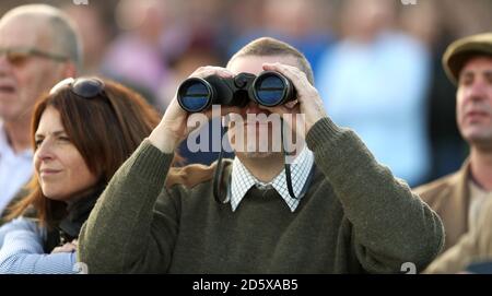 A racegoer watches the action through binoculars during day one of the Showcase at Cheltenham Racecourse Stock Photo